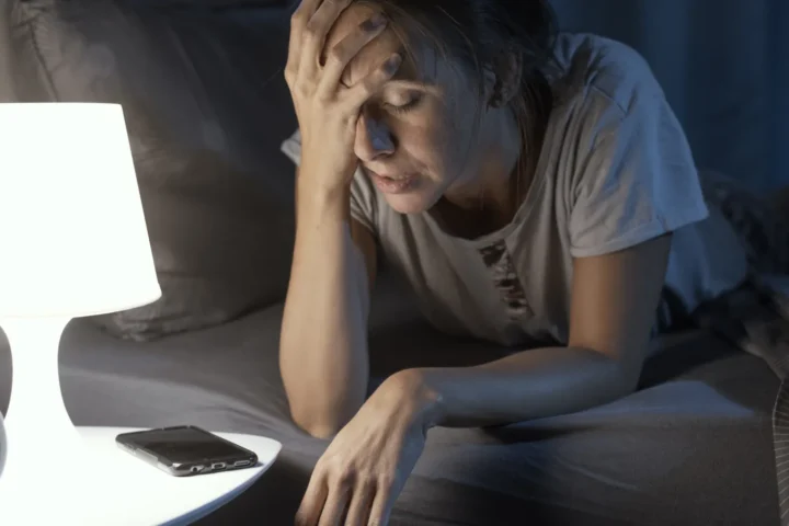 Kobieta siedząca nocą przy laptopie obok lampy i budzika
