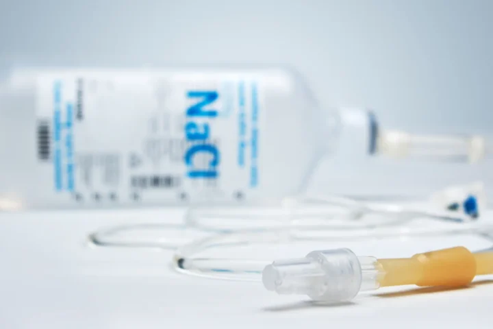 Butelka NaCl, ampułka i przewód zestawu infuzyjnego na jasnym tle